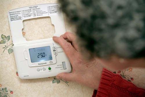 A photograph of a lady looking at her heating controls